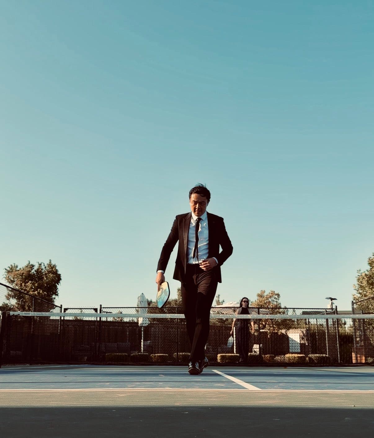Geoff Woo in a suit walking across a padel court